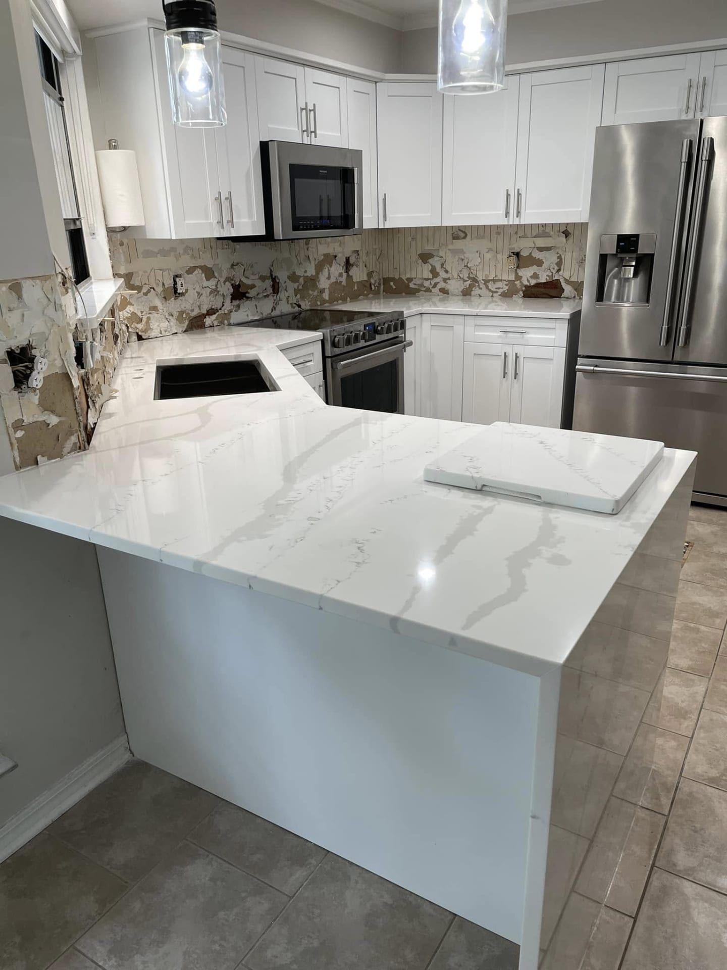 White kitchen with thick waterfall island countertop and polished floor tile